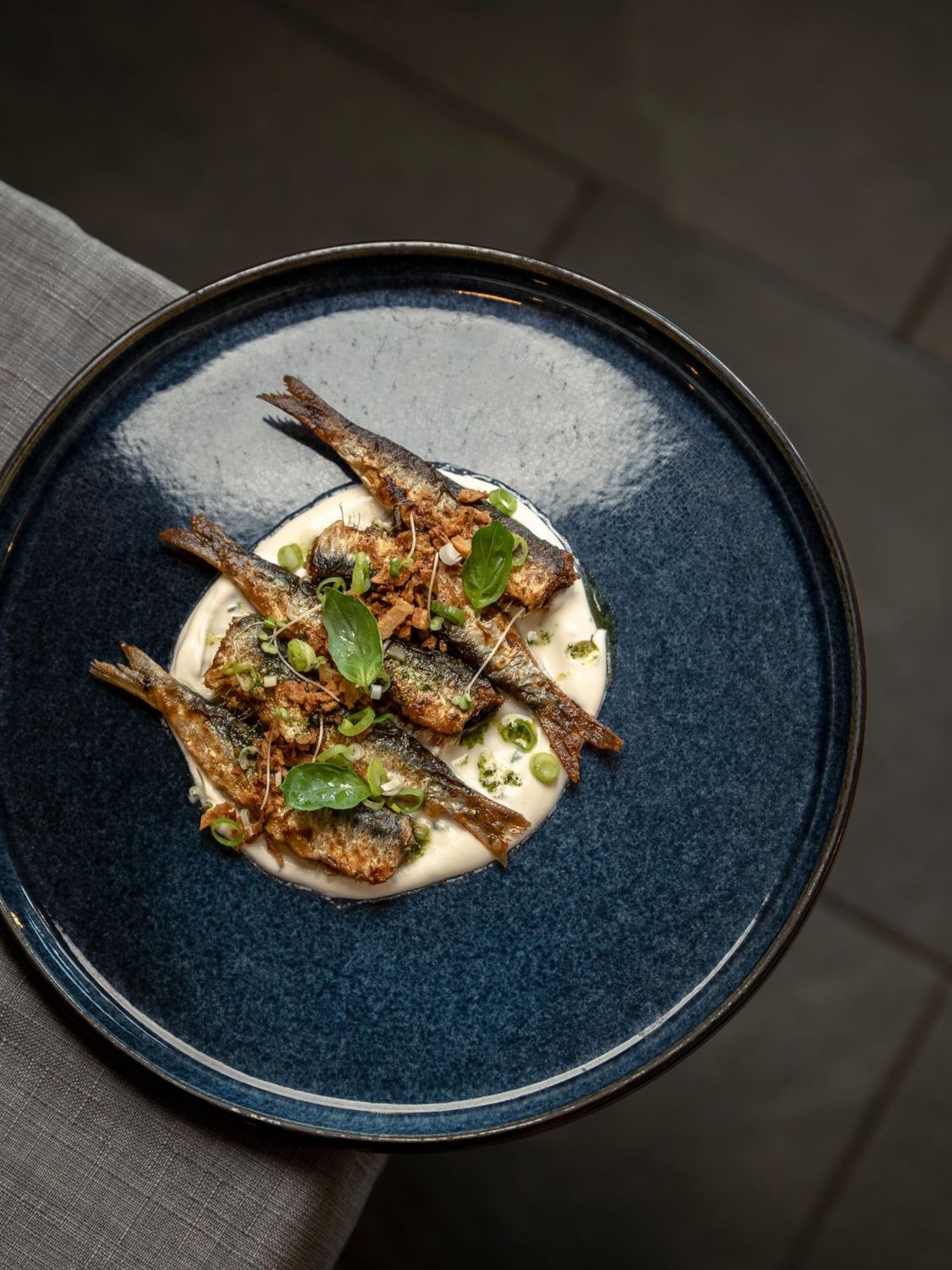 Sardines dressées sur une crème, dans une assiette bleu nuit