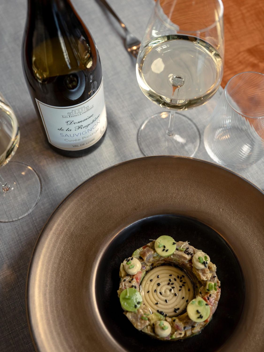Une assiette servie avec une bouteille de vin blanc et deux verres