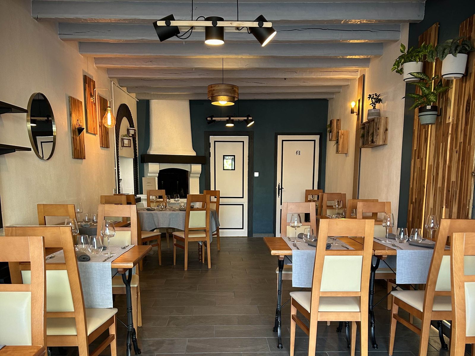 La salle du restaurant : poutres blanches, cheminée et mur bleu pétrole
